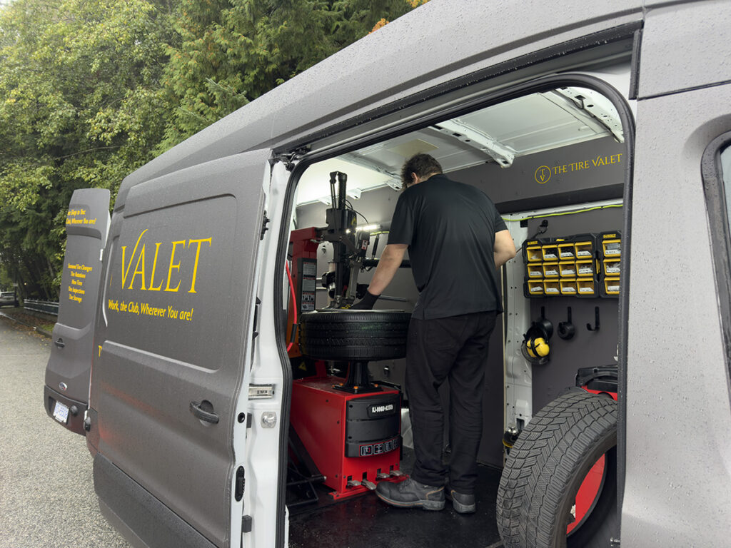 A technician operating a heavy-duty tire mounting and balancing machine inside a clean, organized "The Tire Valet" mobile service van.