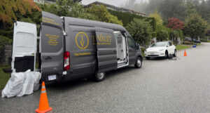 A "The Tire Valet" mobile tire repair van performing on-site tire installation and balancing for a white Tesla Model Y in a residential West Vancouver neighborhood.