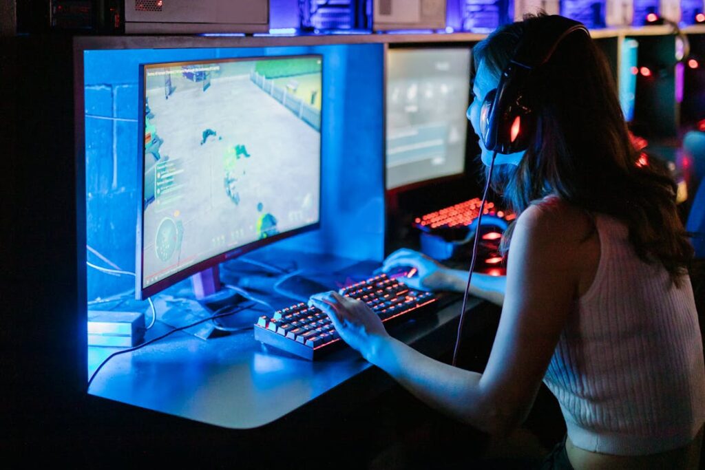 Female gamer at a computer with headphones and RGB keyboard, representing the modern computer game boosting industry