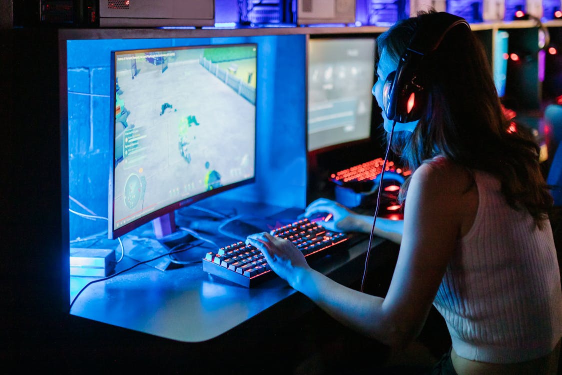 Female gamer at a computer with headphones and RGB keyboard, representing the modern computer game boosting industry