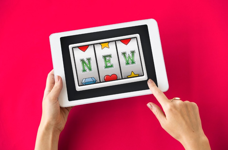 Hand holding a tablet showing a slot reel spelling NEW